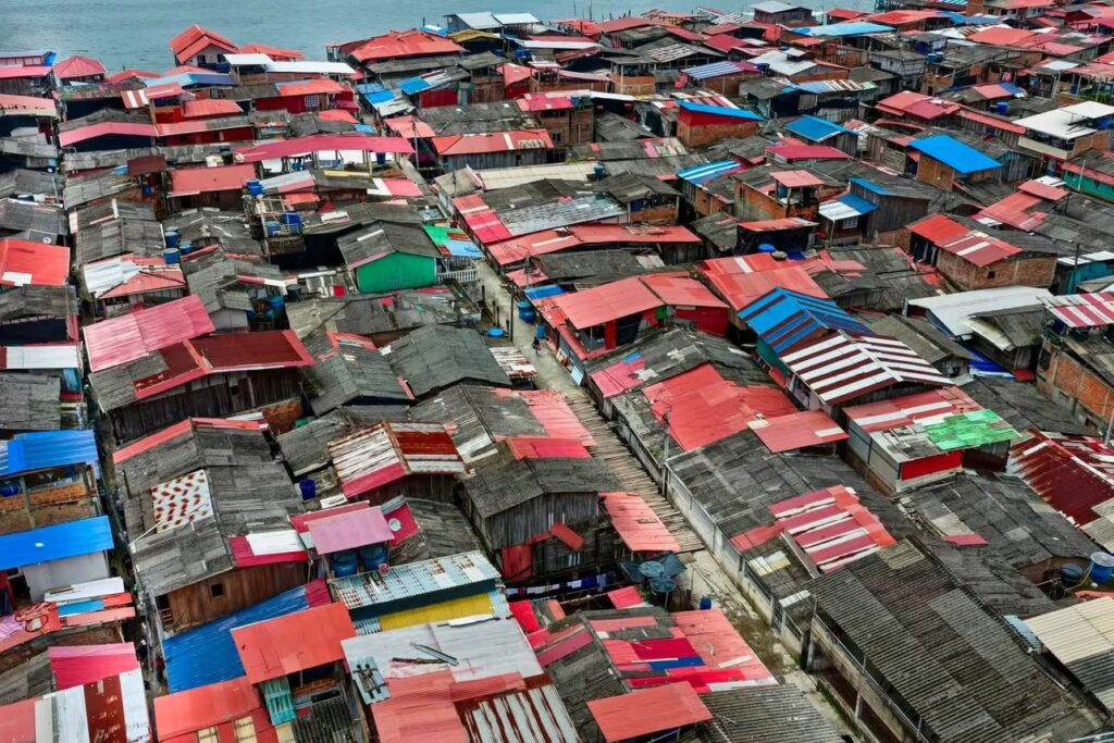 Vista aérea de un denso sector urbano palafítico en la zona de bajamar con techos de lámina y puentes de madera.