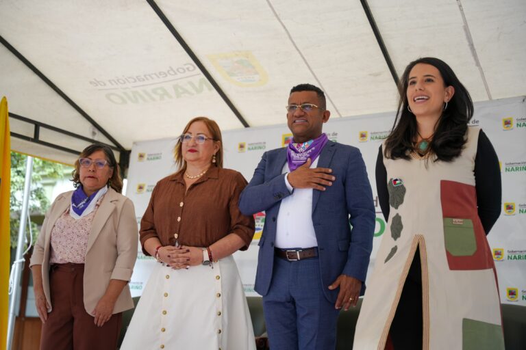 El Gobernador de Nariño y tres funcionarias de pie en una tarima institucional, con actitud solemne durante un acto protocolario.