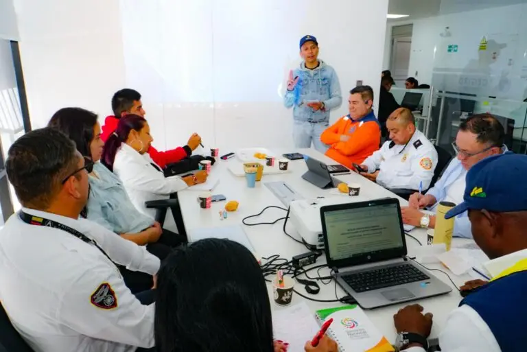Mesa de trabajo conformada por representantes de organismos de socorro y funcionarios gubernamentales discutiendo la ruta departamental del simulacro proyectada en una pantalla y un computador.