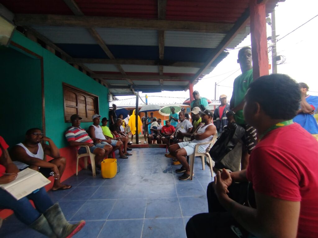 Fotografía de un grupo de habitantes de las comunidades de Sanquianga o Francisco Pizarro reunidos en un corredor techado, sentados en sillas plásticas y conversando durante un encuentro comunitario.