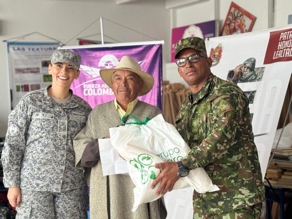 Integrantes de la Fuerza Aérea Colombiana y del Ejército Nacional entregan un paquete de ayuda a un adulto mayor durante una jornada comunitaria.