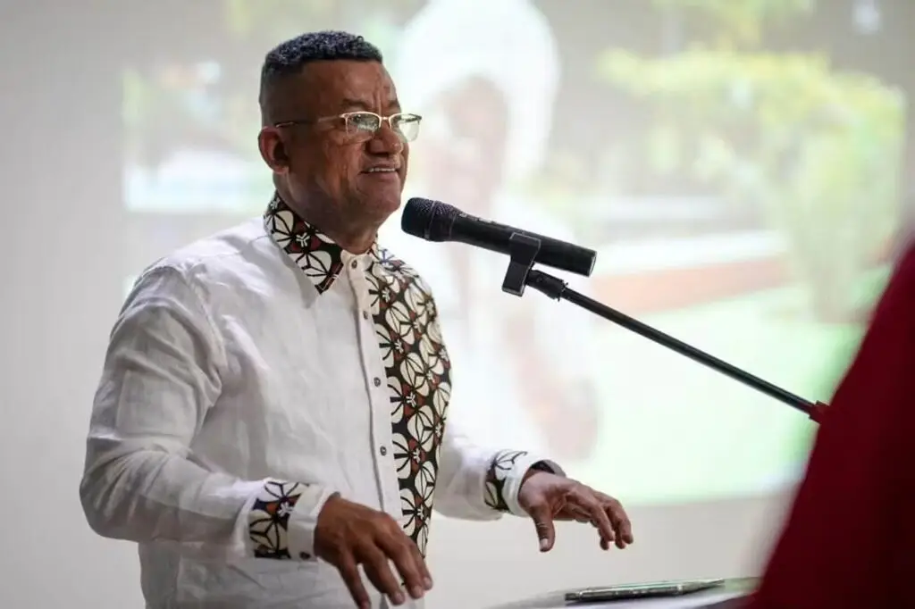El Gobernador de Nariño hablando por un micrófono durante la Asamblea Pública de Elección, vistiendo una camisa blanca con detalles estampados.