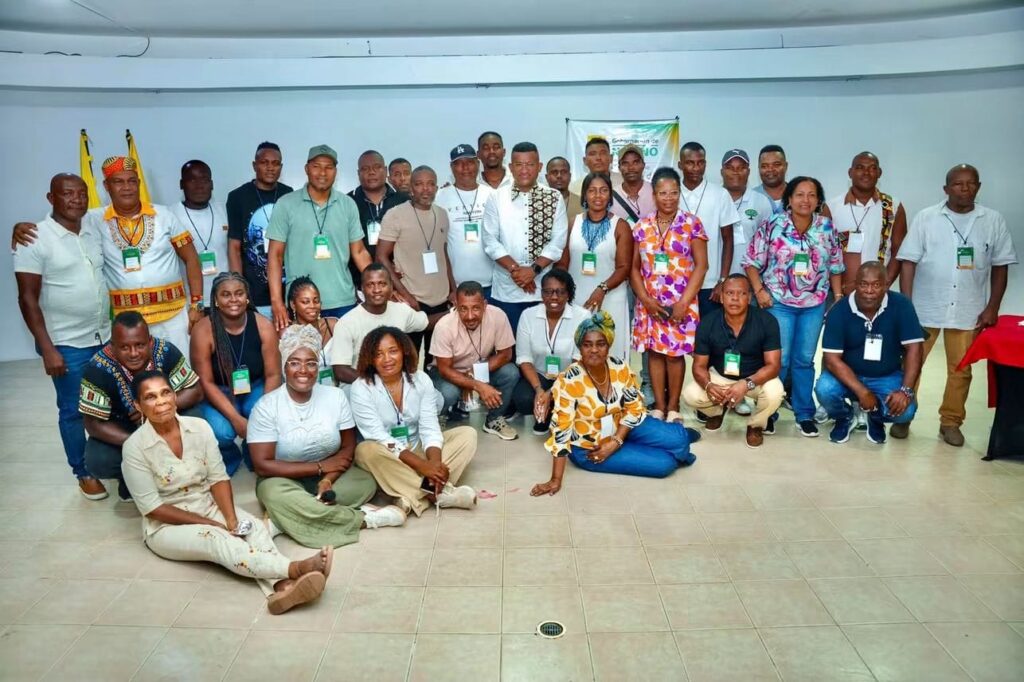 Grupo de hombres y mujeres afrodescendientes posando sonrientes junto al Gobernador de Nariño en un salón de eventos tras una jornada de elección.