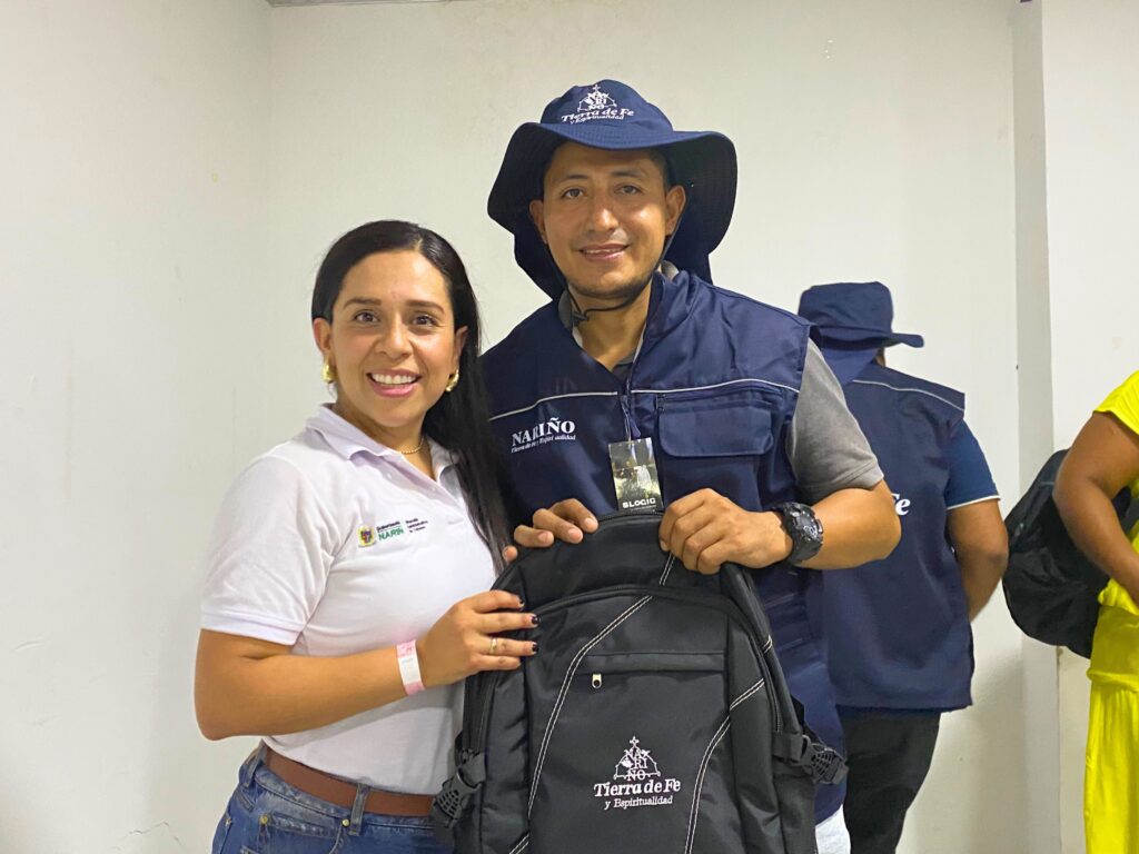 Representante institucional entrega una mochila y elementos de trabajo a un guía profesional de turismo de Tumaco, quien porta chaleco y sombrero de la estrategia Nariño Tierra de Fe y Espiritualidad.
