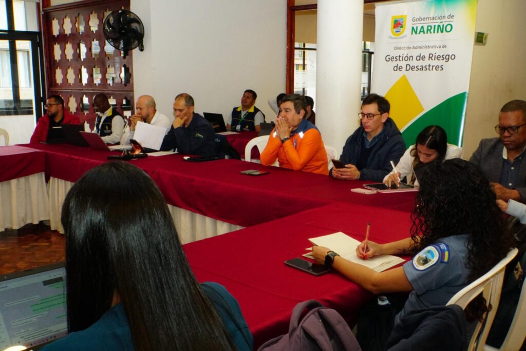 Miembros del Consejo Departamental para la Gestión del Riesgo de Desastres reunidos alrededor de una mesa institucional analizando documentos en Pasto.