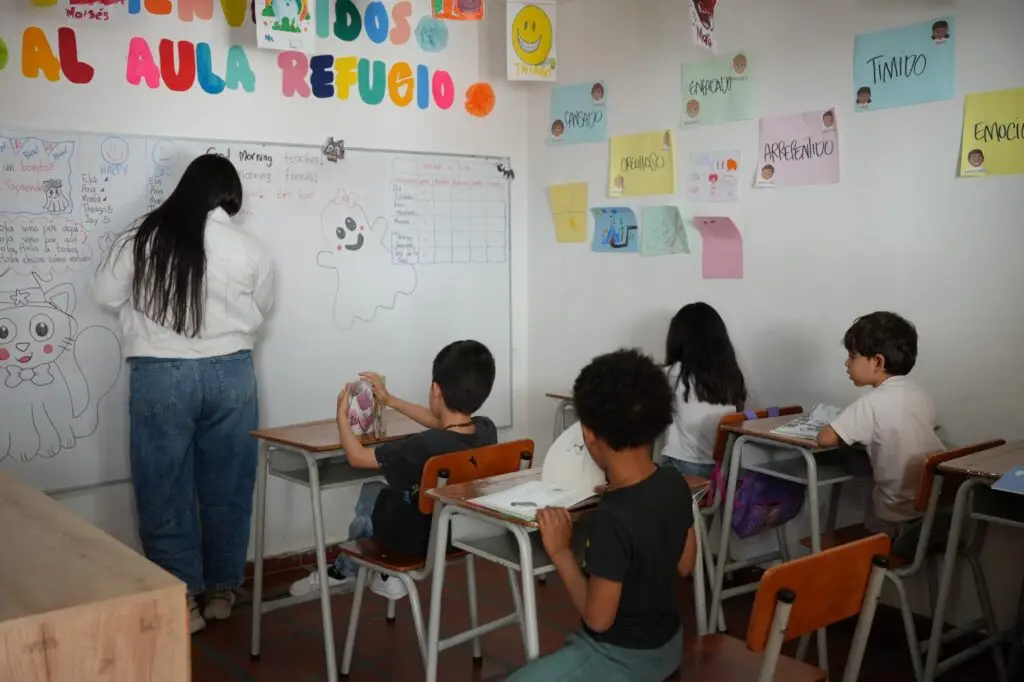 Niñas y niños participan en una actividad pedagógica dentro de un aula, acompañados por una orientadora que desarrolla ejercicios sobre emociones y convivencia.