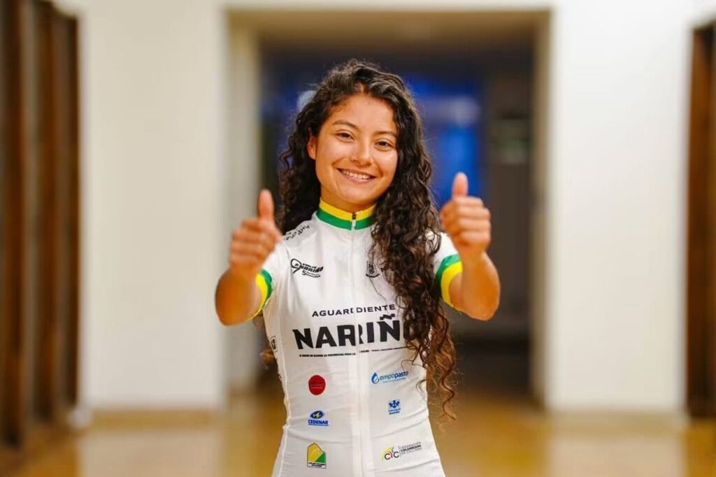 Joven ciclista sonriente levantando ambos pulgares en señal de aprobación, vistiendo el jersey blanco oficial con los logos de Aguardiente Nariño y otros patrocinadores de la Vuelta a Nariño.