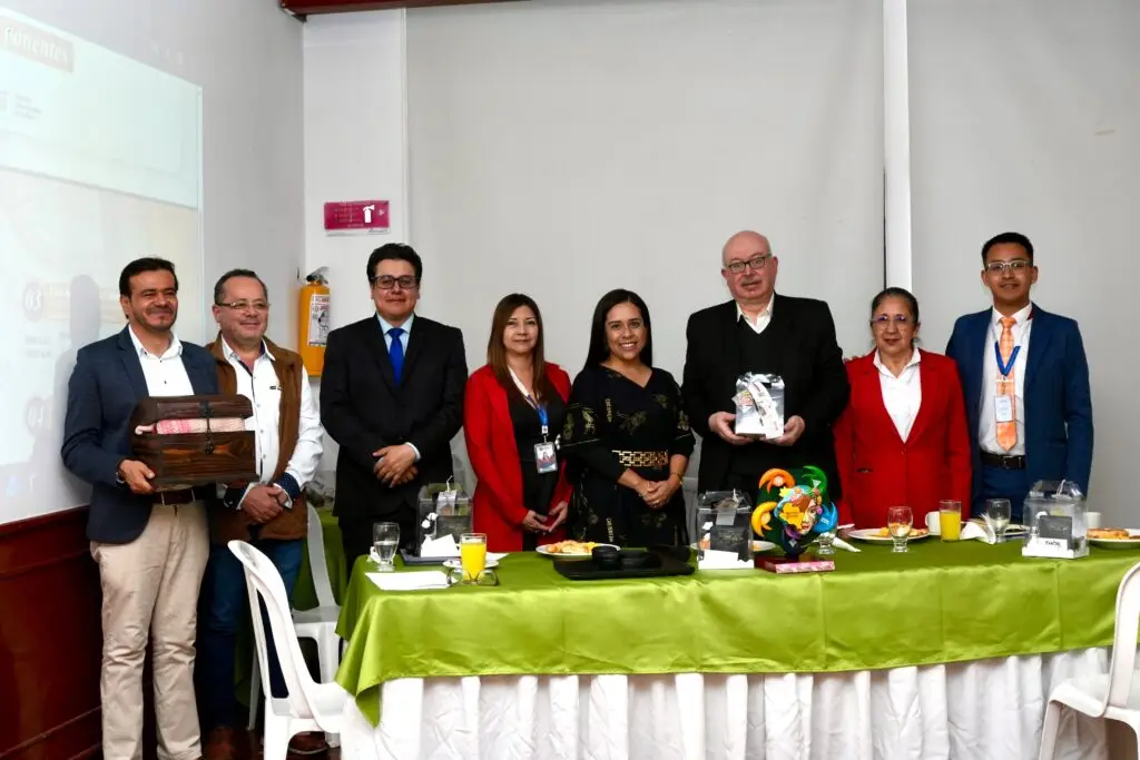 Grupo de ocho personas posando sonrientes detrás de una mesa con mantel verde, sosteniendo obsequios y una artesanía representativa durante un evento oficial.