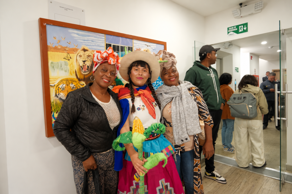 Tres mujeres posan durante una actividad cultural realizada en la Biblioteca Pública Departamental de Nariño; una de ellas viste indumentaria tradicional y sostiene una figura artesanal de maíz.