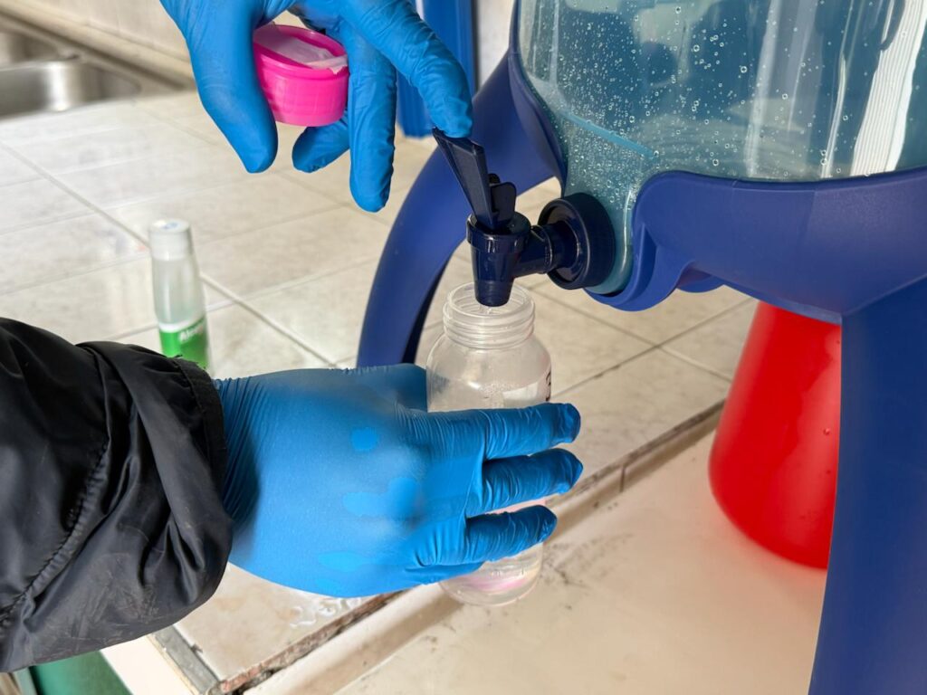 Persona con guantes dispensa agua desde un filtro en un recipiente, como parte de acciones para mejorar el acceso a agua segura en Nariño.