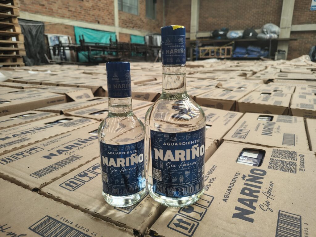 Dos botellas de Aguardiente Nariño Sin Azúcar en diferentes presentaciones, dispuestas sobre cajas de cartón apiladas en una bodega de almacenamiento.