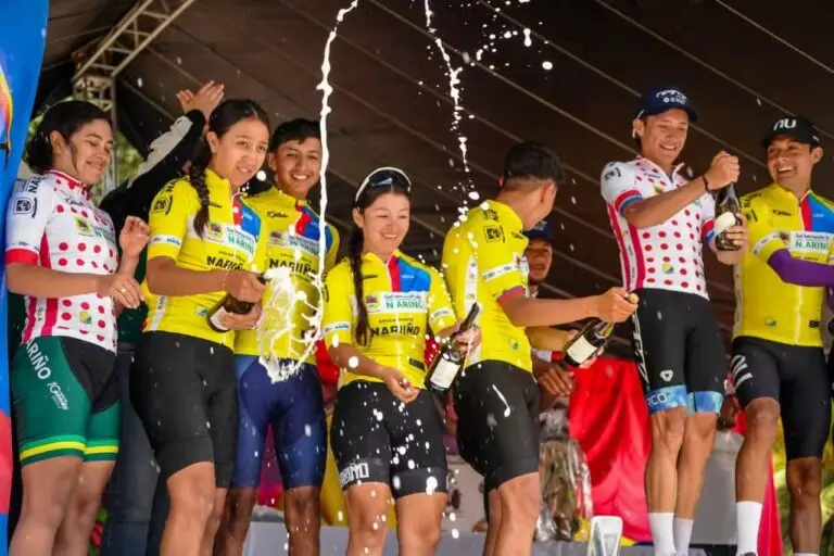 Ciclistas de la Décima Vuelta a Nariño celebran en el podio durante la premiación, con uniformes de sus equipos y botellas de champaña.