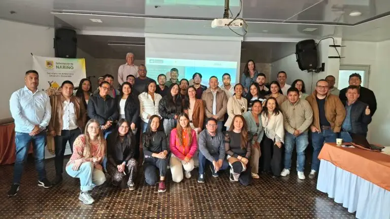 Grupo numeroso de personas posando sonrientes para una fotografía en un salón de eventos, acompañados de un pendón oficial de la Secretaría de Ambiente y Desarrollo Sostenible de la Gobernación de Nariño.