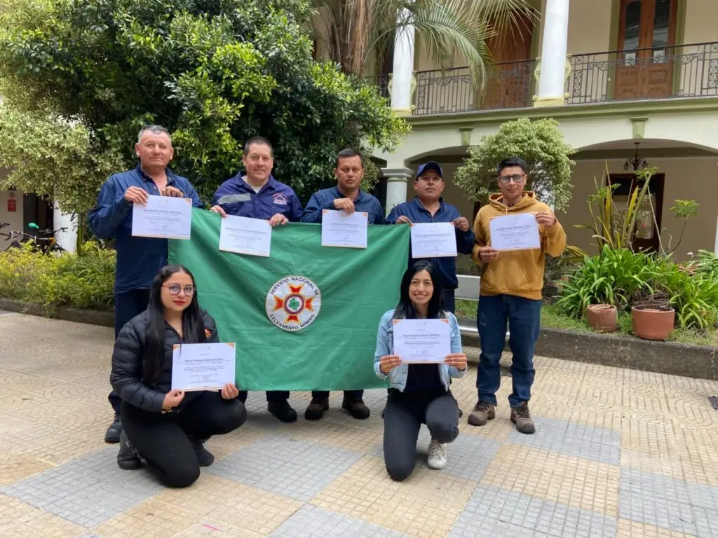 Participantes del Curso de Coordinador Logístico de Salvamento Minero posan con sus certificados y una bandera del Servicio Nacional de Salvamento Minero.