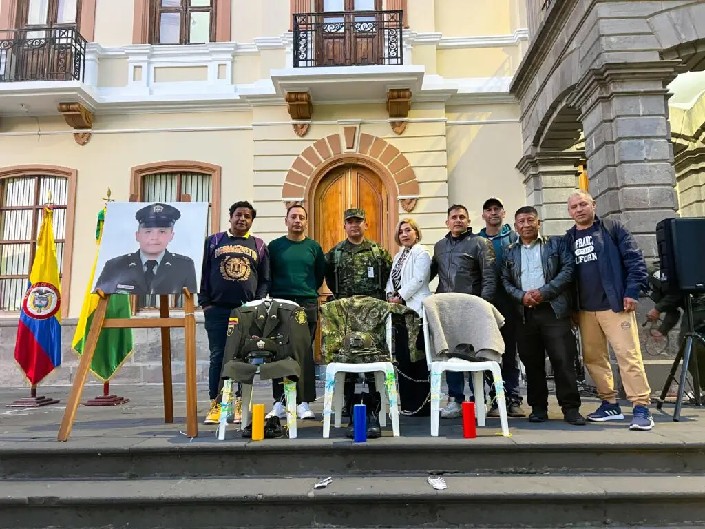 Integrantes de la Fuerza Pública y ciudadanos participan en un homenaje frente a una fotografía y uniformes dispuestos en memoria de personas afectadas por el conflicto.