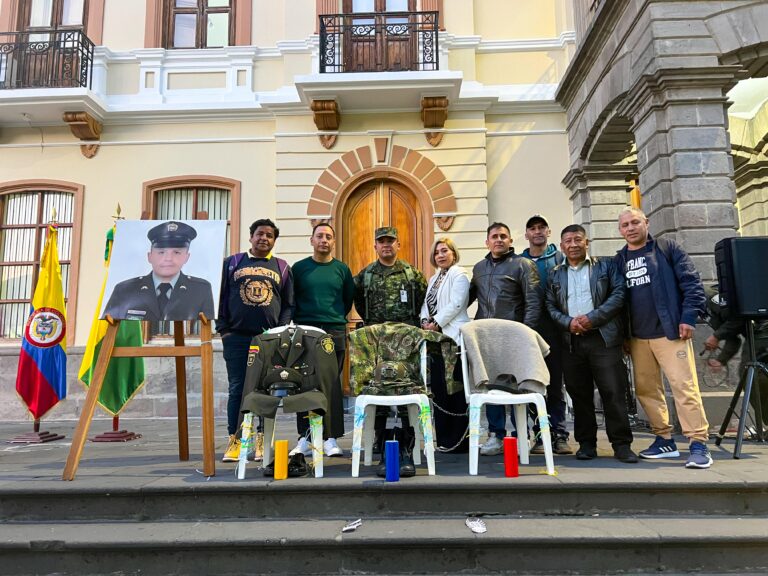 Integrantes de la Fuerza Pública y ciudadanos participan en un homenaje frente a una fotografía y uniformes dispuestos en memoria de personas afectadas por el conflicto.