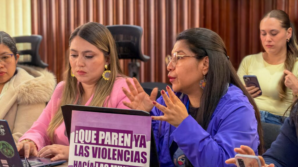 Mujeres participan en una sesión sobre prevención de las violencias basadas en género, junto a un cartel con el mensaje “¡Que paren ya las violencias!”