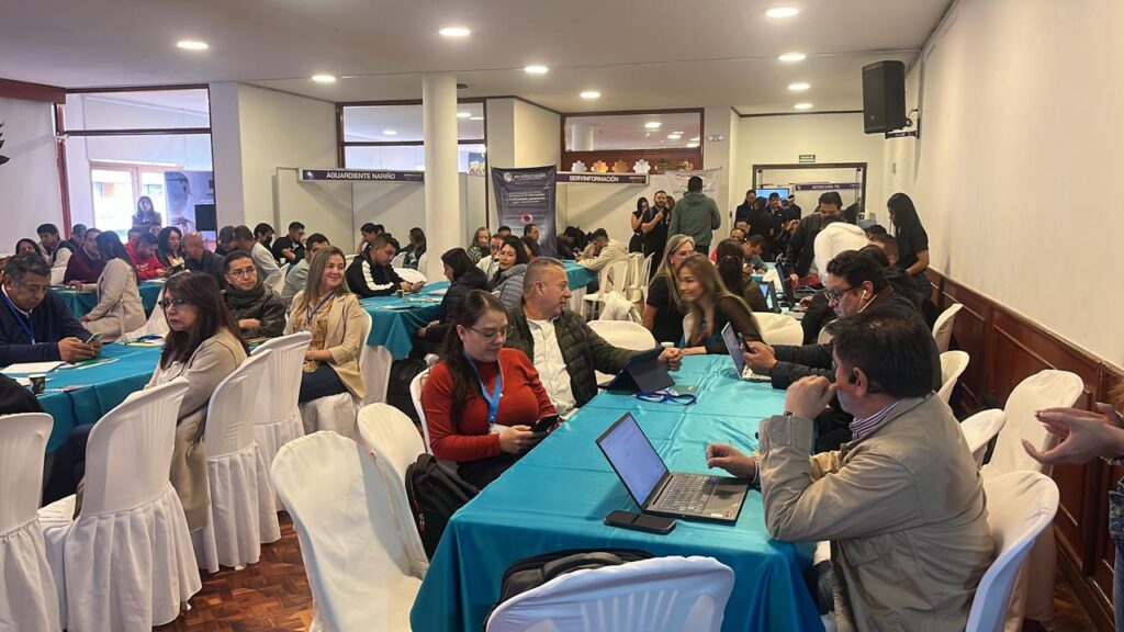 Funcionarios y participantes trabajan en mesas con computadores y dispositivos durante una jornada de tecnología e innovación en Nariño.