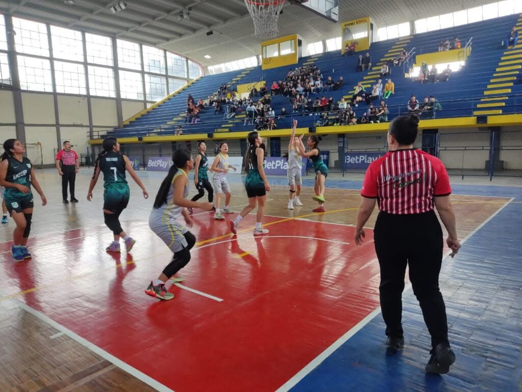 Jugadoras participan en un partido de baloncesto femenino en un coliseo de Nariño, mientras público y jueces acompañan la competencia.