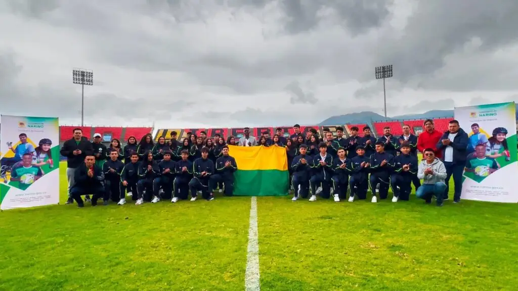 Delegación de deportistas y representantes institucionales posa en un estadio con una bandera de Nariñ