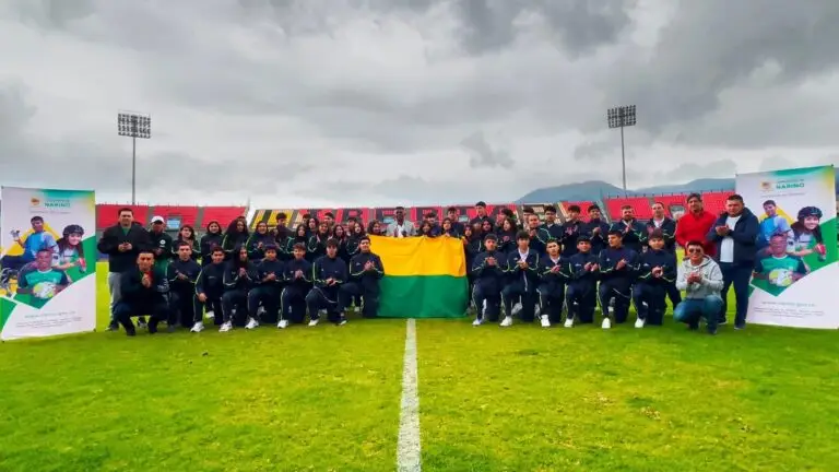 Delegación de deportistas y representantes institucionales posa en un estadio con una bandera de Nariñ