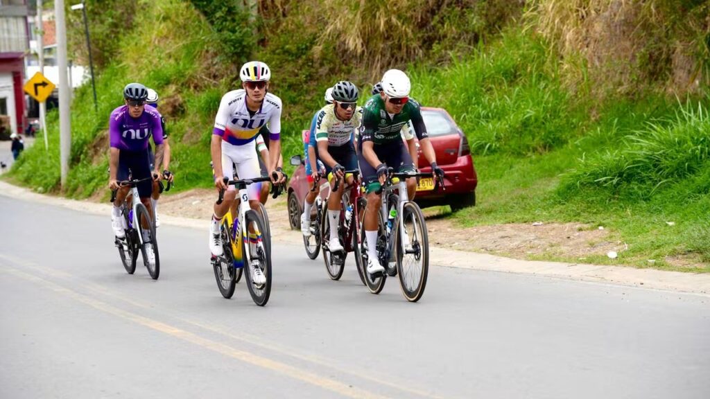 Grupo de ciclistas avanza por una carretera rodeada de vegetación durante la Décima Vuelta a Nariño.