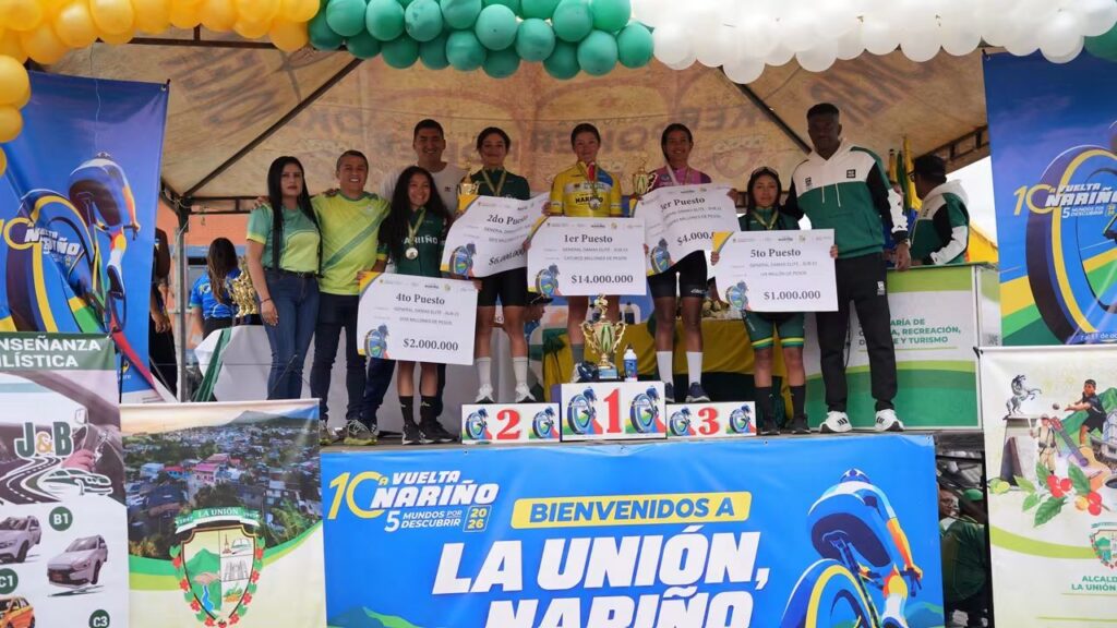 Ciclistas femeninas y representantes de la organización posan en el podio de premiación de la Décima Vuelta a Nariño en La Unión, con trofeos y carteles de reconocimiento económico.
