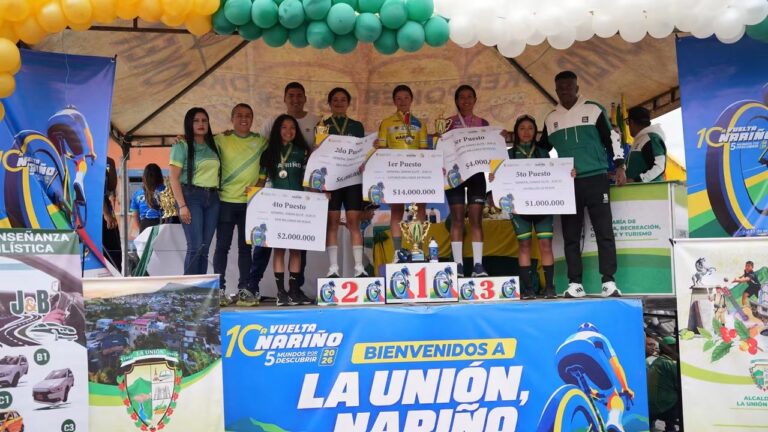 Ciclistas femeninas y representantes de la organización posan en el podio de premiación de la Décima Vuelta a Nariño en La Unión, con trofeos y carteles de reconocimiento económico.
